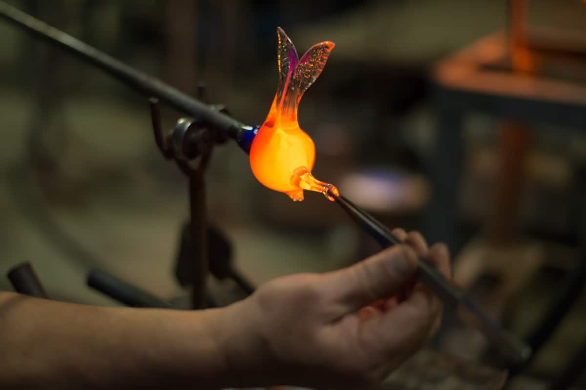 A glass maker making a glass bird figurine with his glass making equipment 