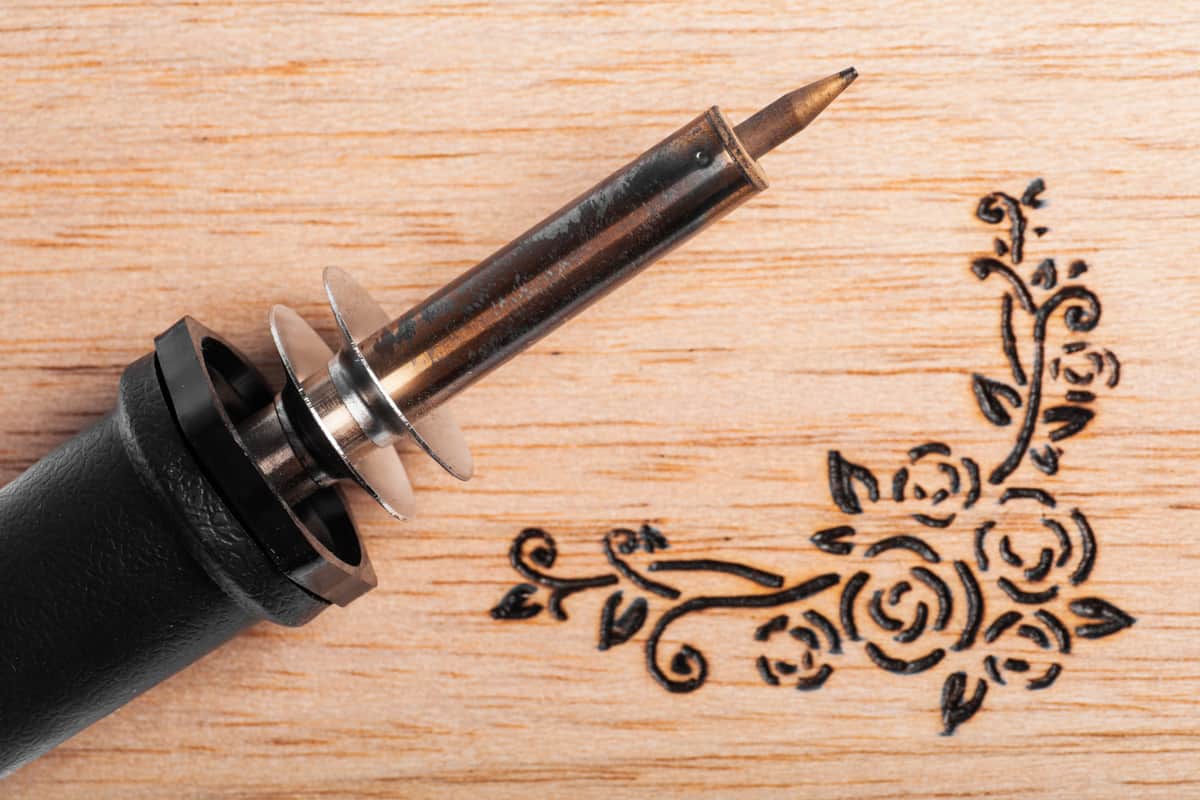 A pyrography pen placed on a wooden board with a pyrography art on the side