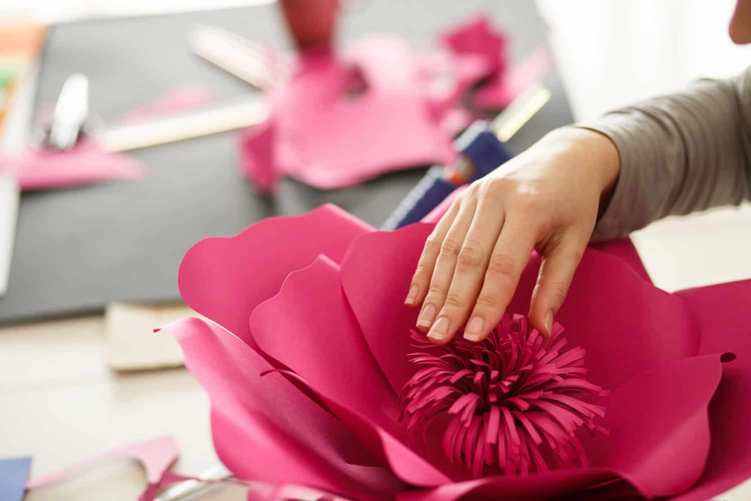 Female creating a beautiful paper flower at her workstation using pink construction paper