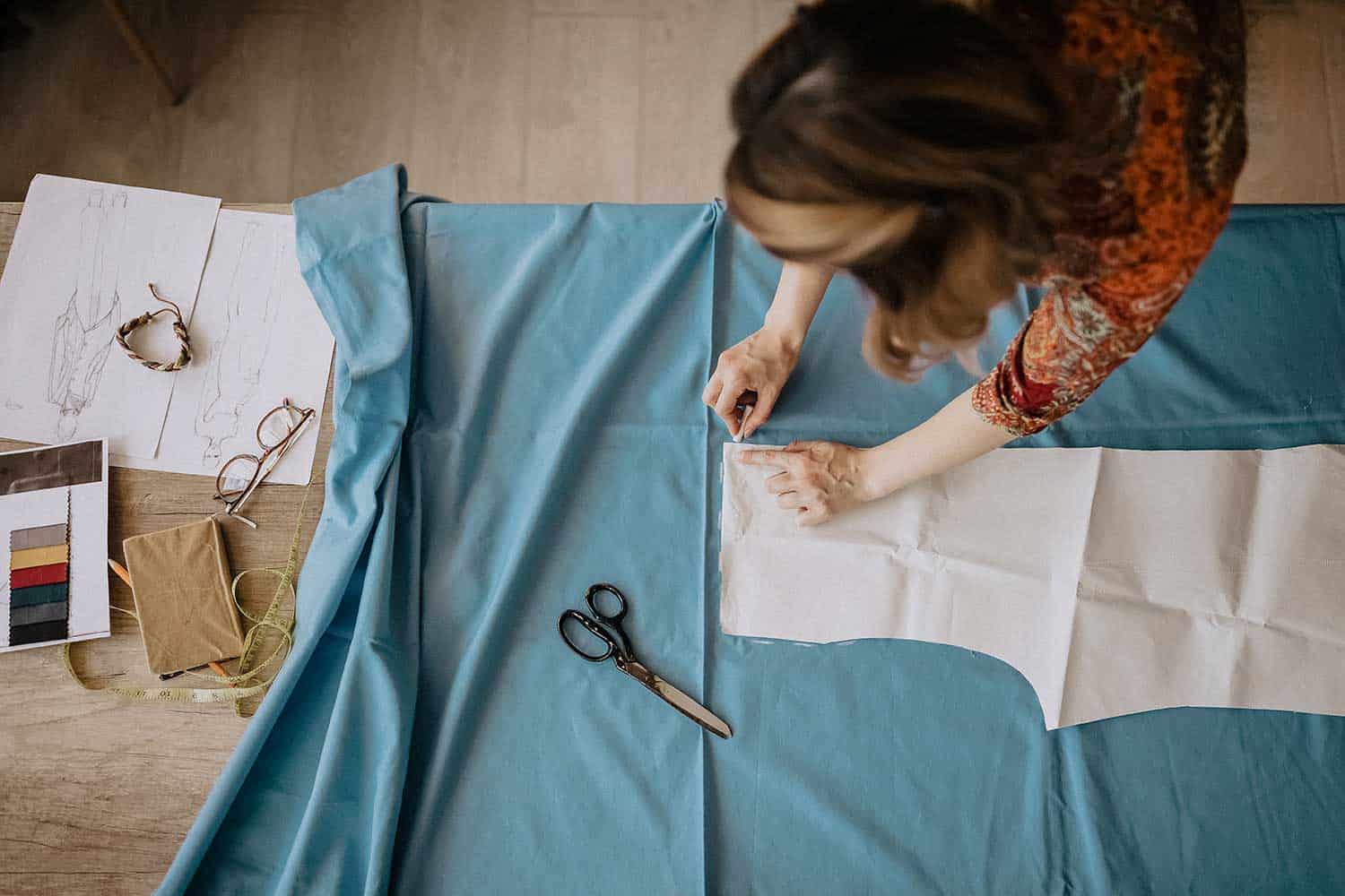 Unrecognizable fashion designer cutting fabric in her design workshop
