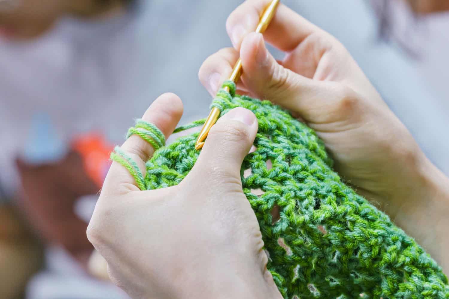 A woman making a scarf using crochet needles and a green yarn