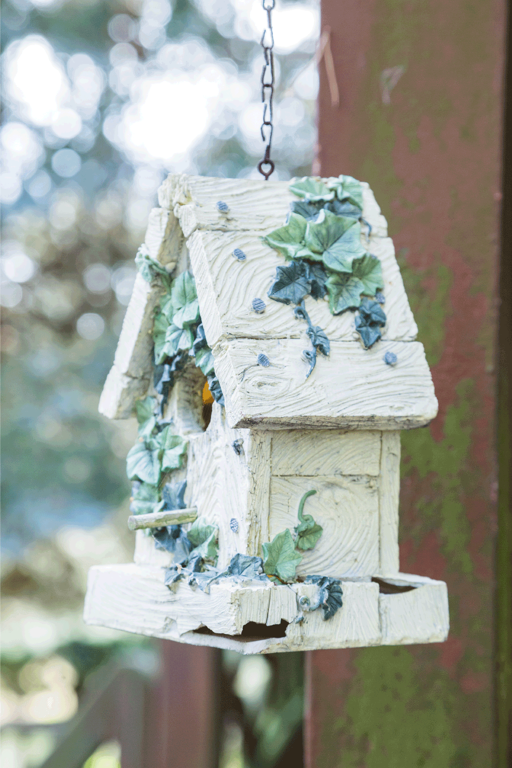 Ornate birdhouse with color stucco leaves hanging on chain with bird inside