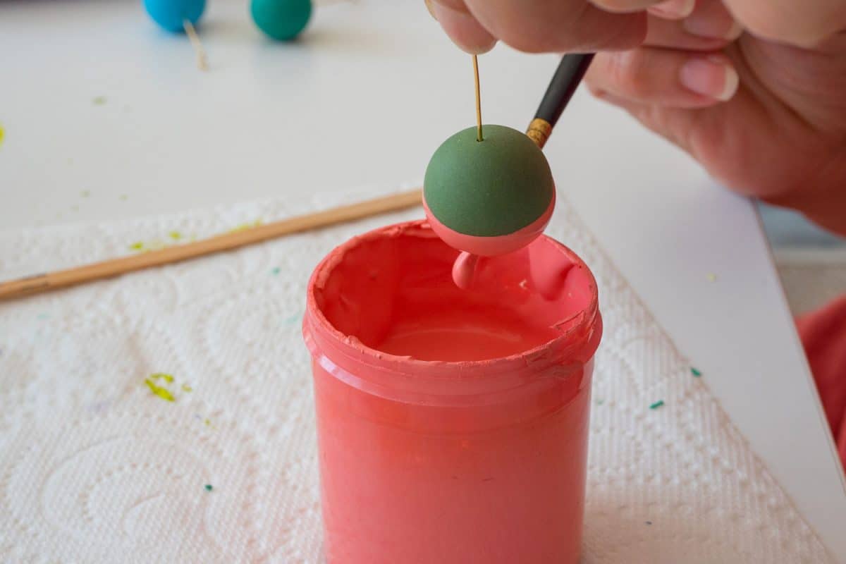 A woman dripping her polymer clay ball into a cup of paint