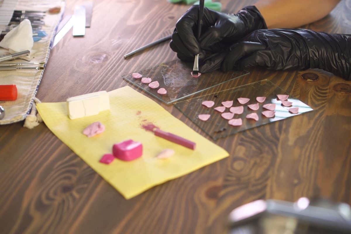 A woman doing a polymer clay work on a glass workpiece on her table