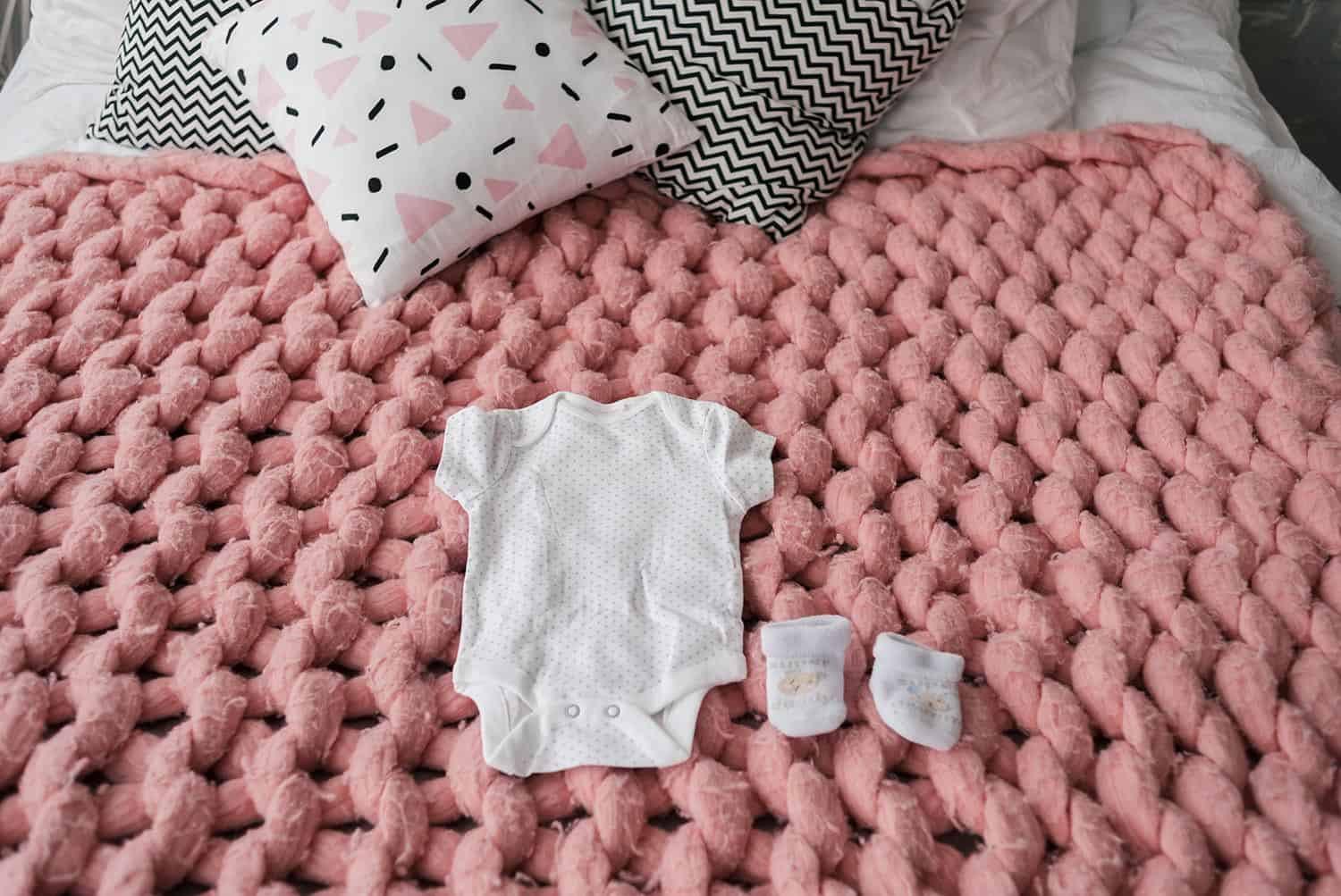 Baby clothes and shoes for newborn in pastel colors on pink merino wool blanket