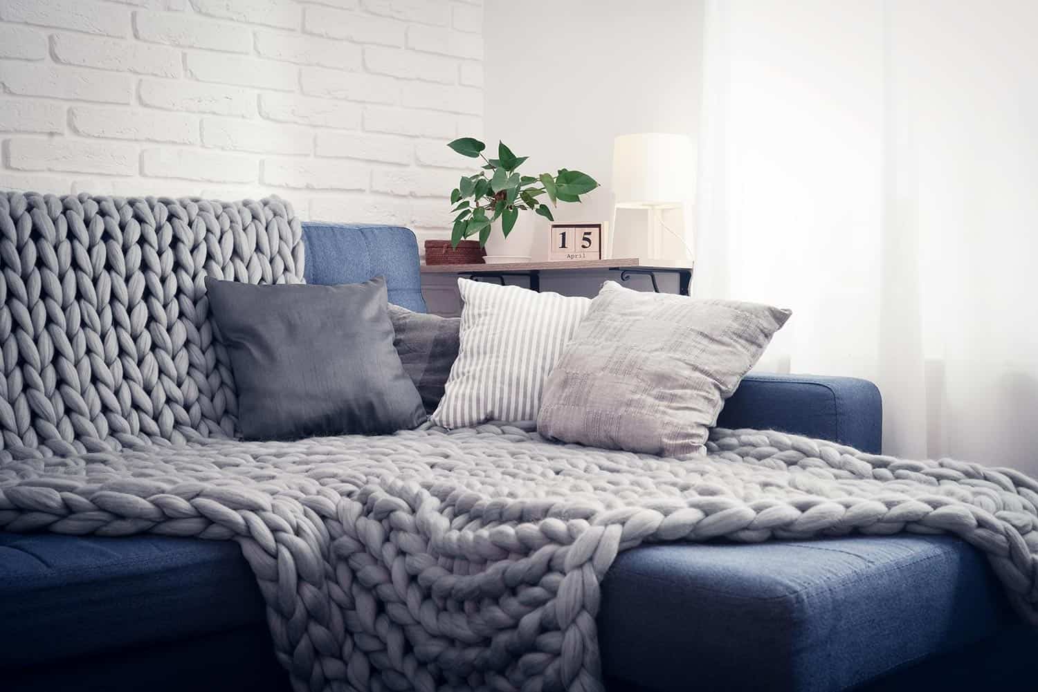 Gray knitted blanket from merino wool on couch with pillows