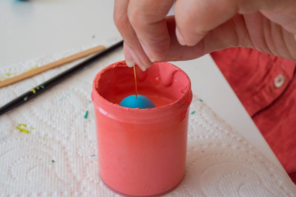 A woman dipping a polymer clay ball into a cup of paint