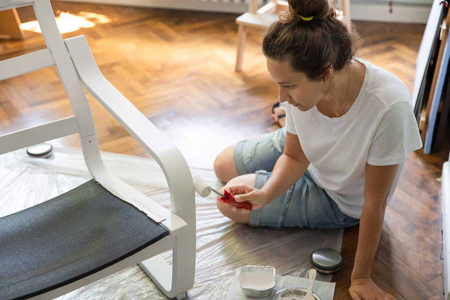 Young woman painting a black wooden chair in white