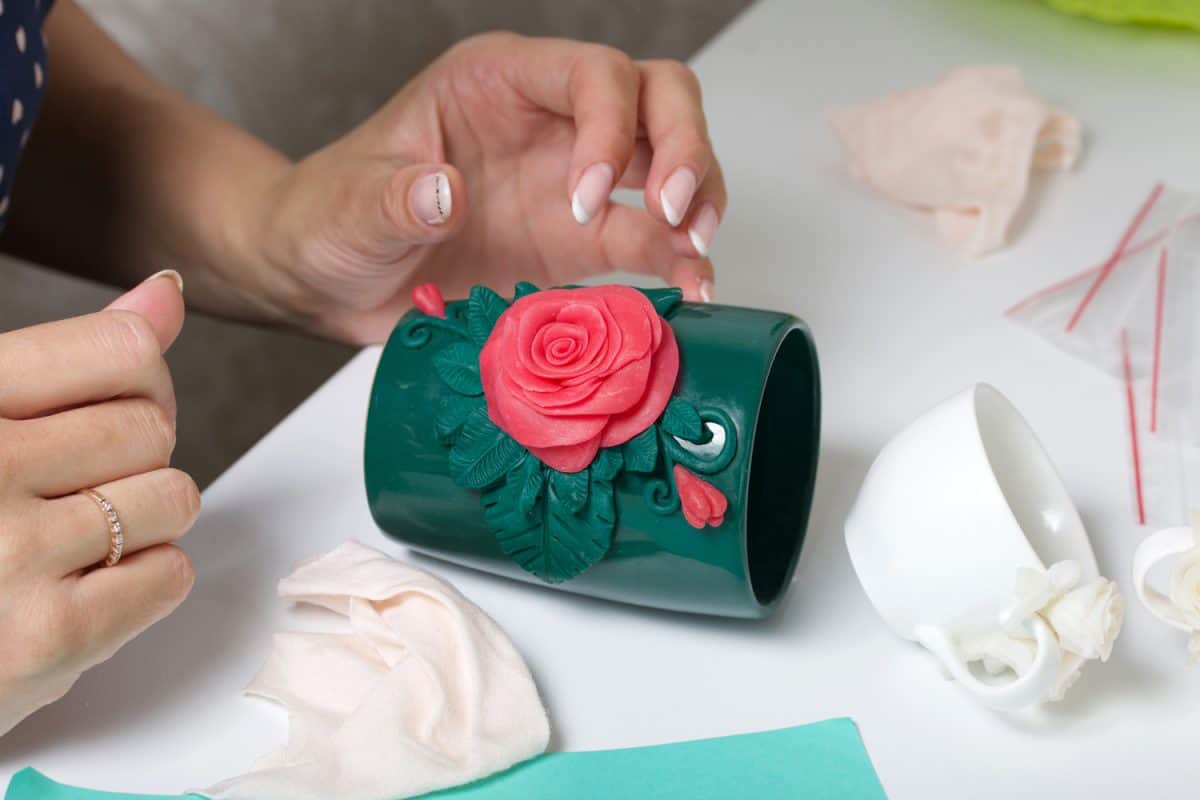 Woman glues polymer clay roses to a mug. Polymer clay of different colors. Crafts from polymer clay.