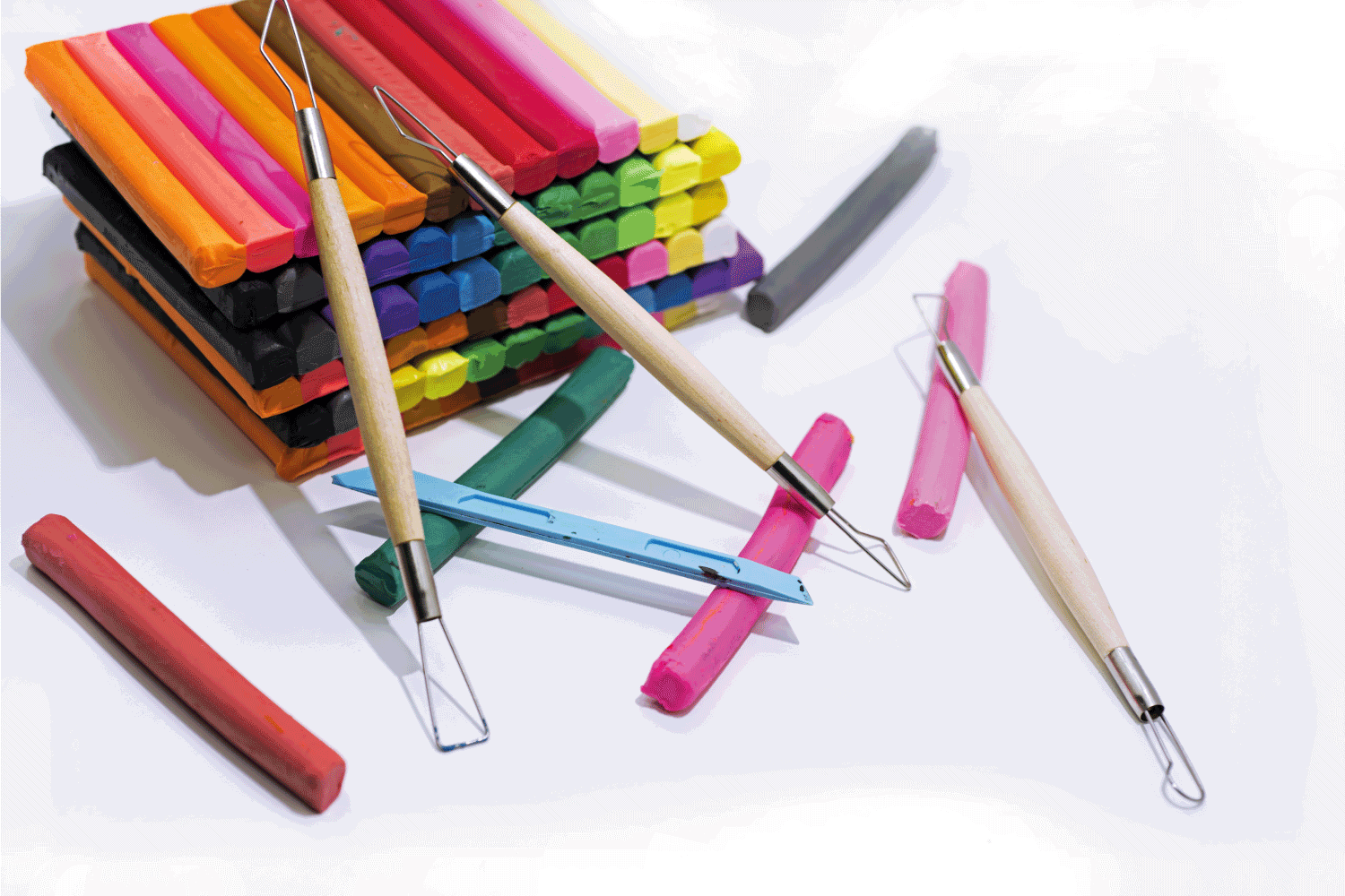 sticks of assorted color of polymer clay and sculpting tools on top of a white table