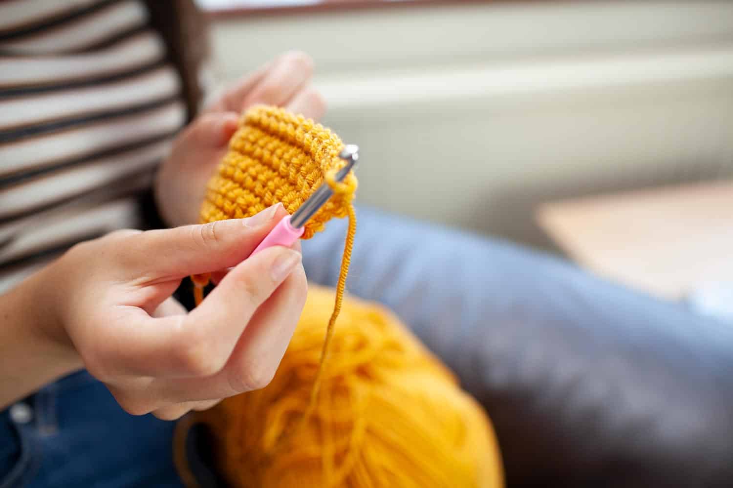 Young woman crocheting with yellow wool
