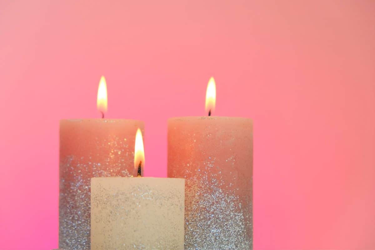 Three tall candles coated with glitter on a pink background
