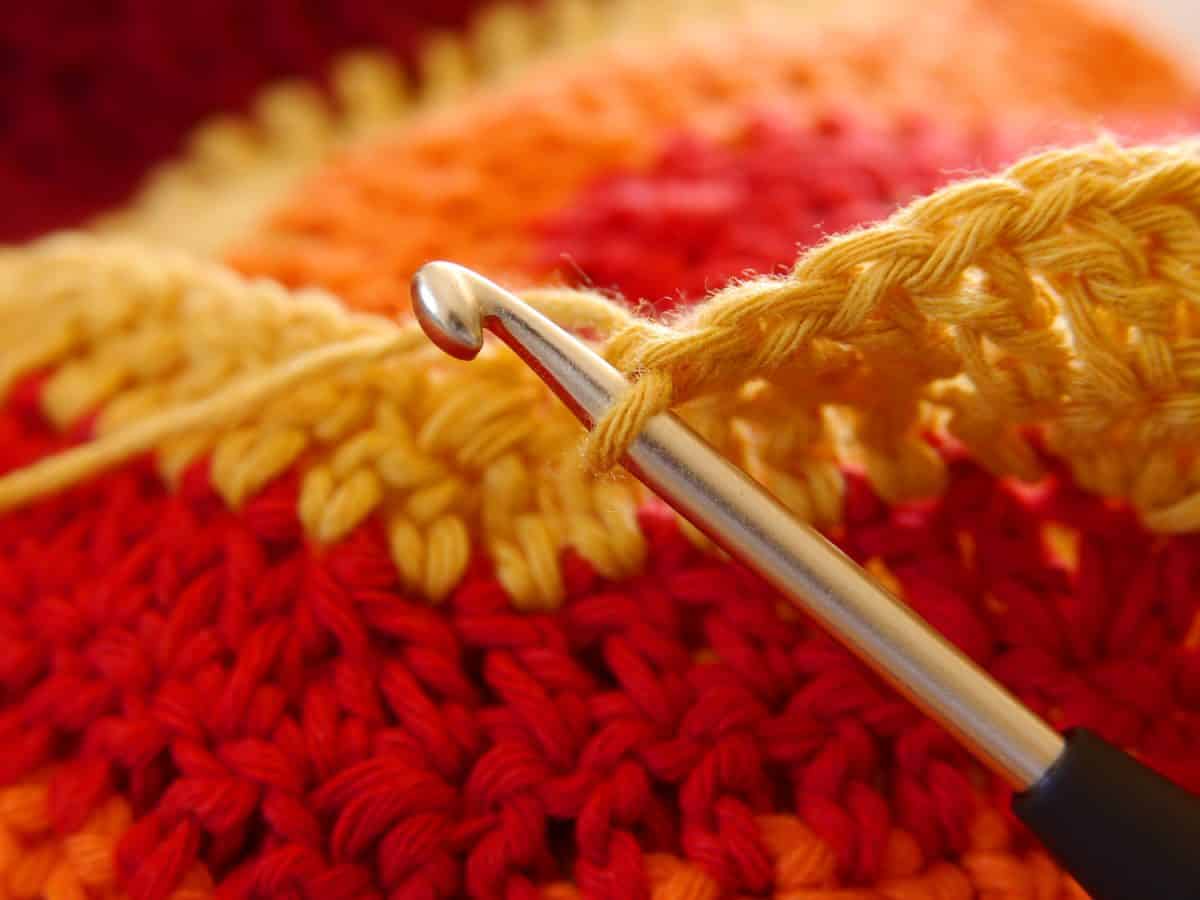 A half-ceiling. Close-up of a crochet hook with wool in various warm shades of red.