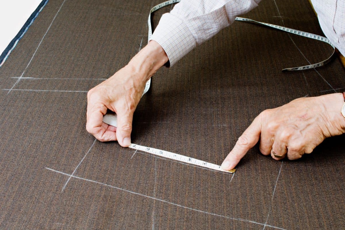 A tailor using a measuring tape and chalk for his markings