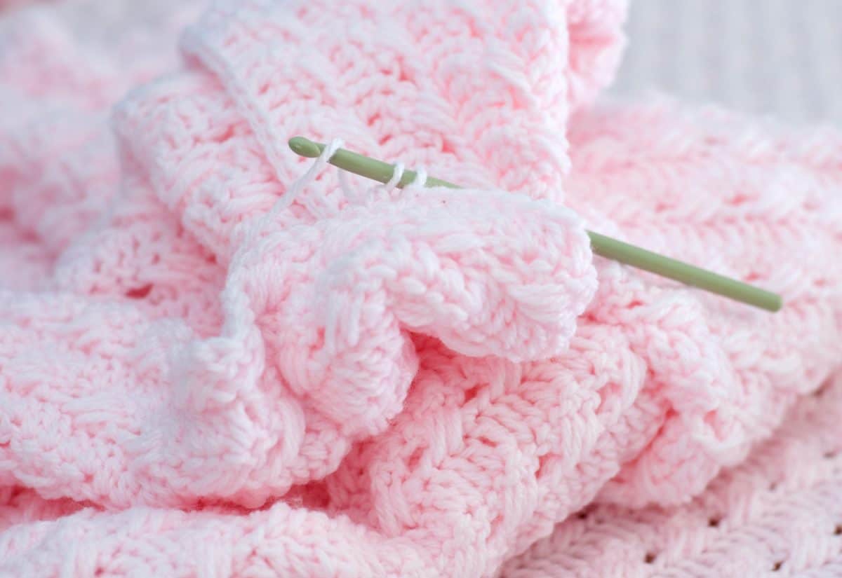 Close-up of crocheted, homemade, baby blanket with crochet hook and yarn