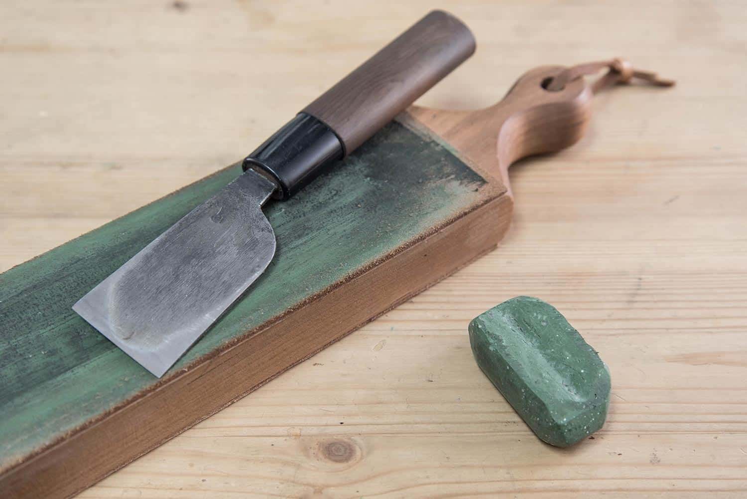 Japanese leather craft knife on a leather knife strop with green polishing compound on a wooden surface