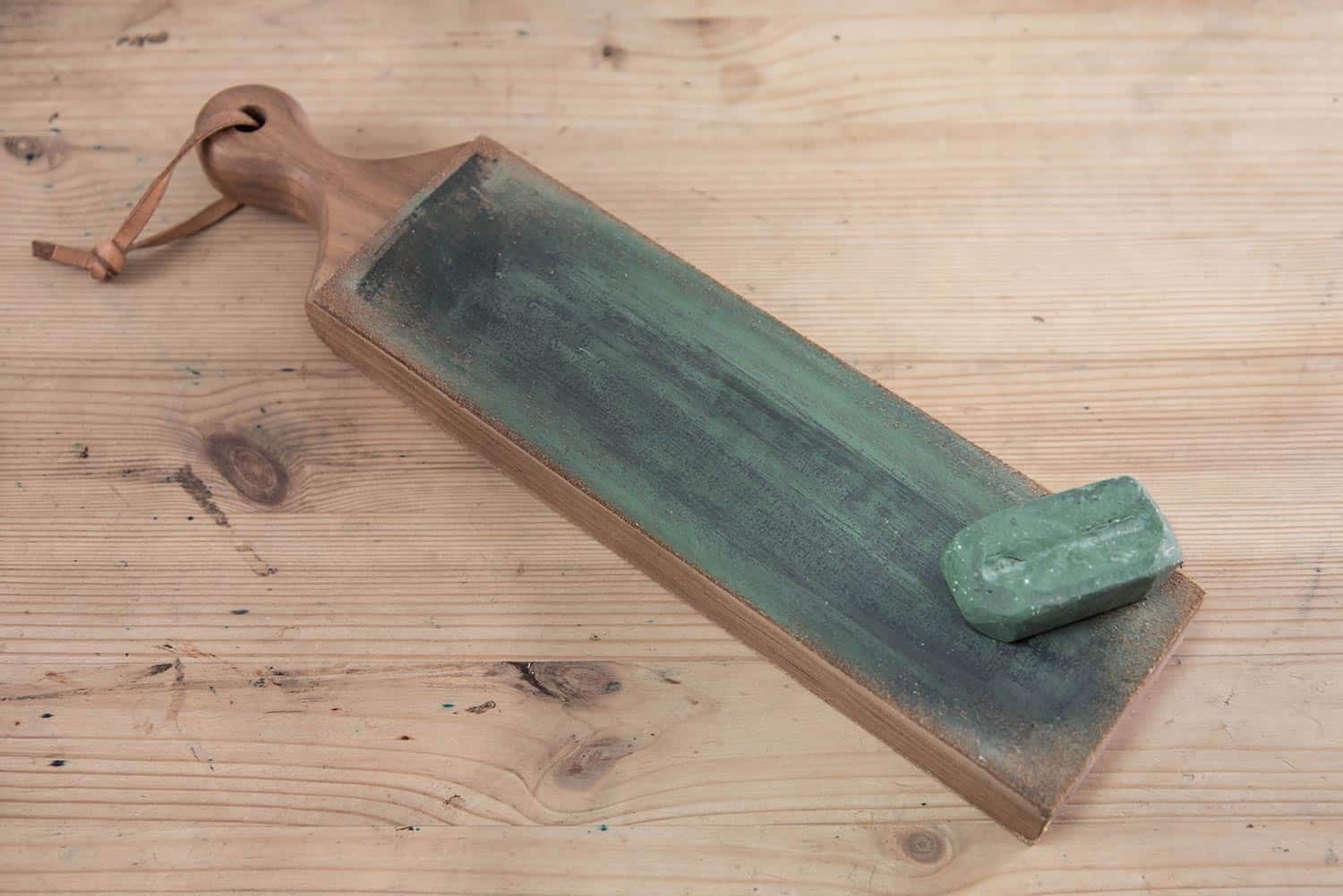 Leather knife strop with green polishing compound on a wooden surface