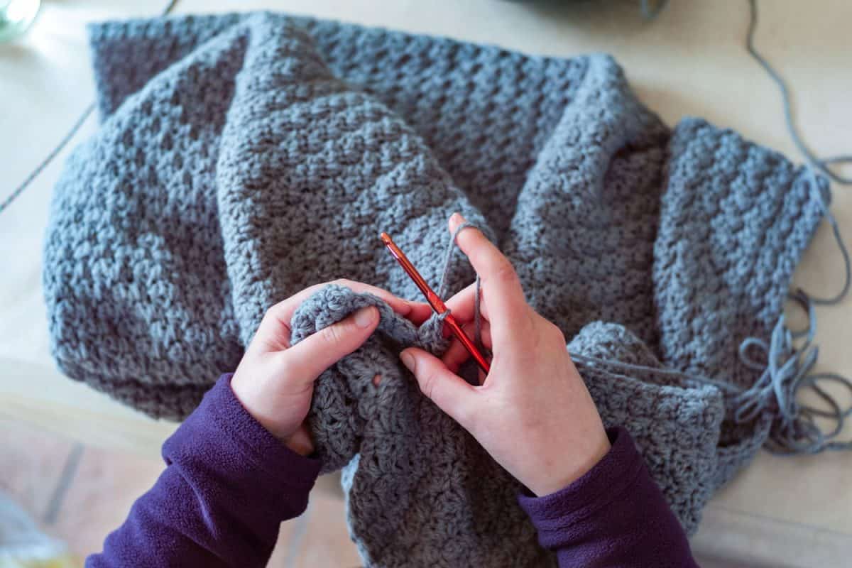 Woman wearing a sweater while crocheting a blue sweater