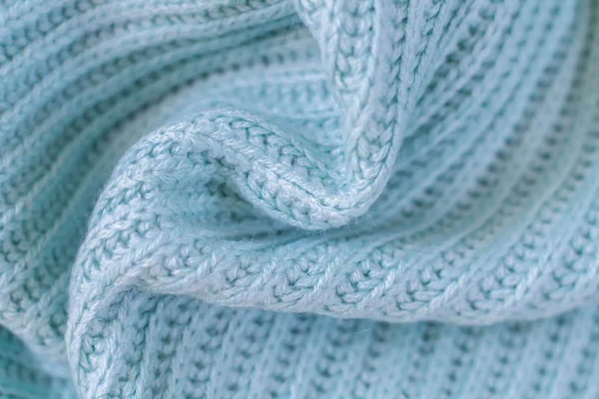 Background of woolen knitted light green blue warm sweater top view