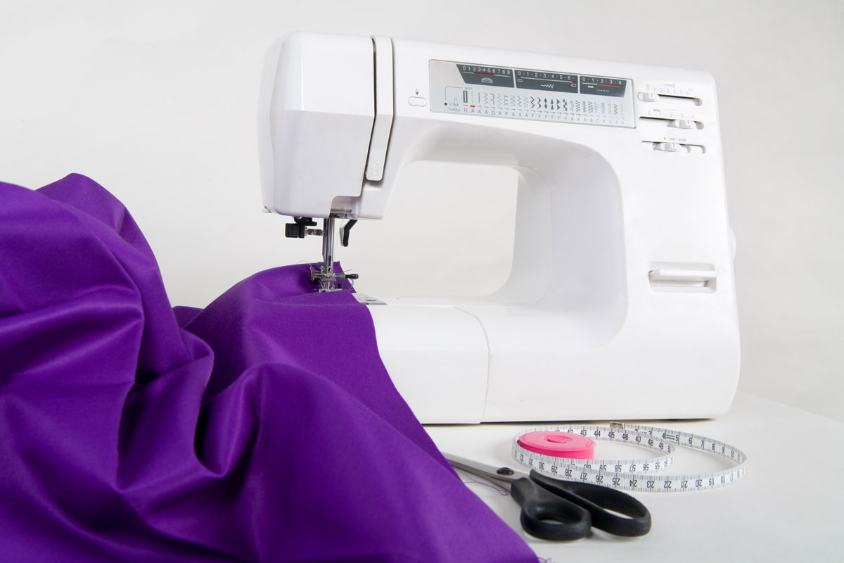 Sewing violet colored fabric and a white sewing machine