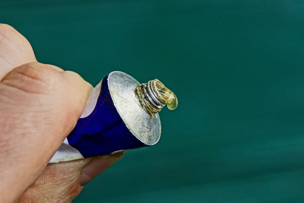 Drop of glue on a tube squeezed in a hand