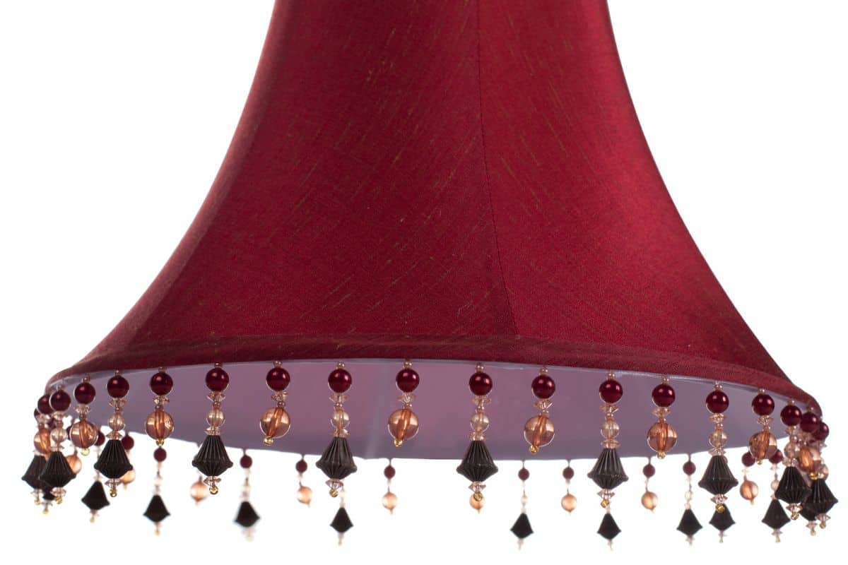 isolated close up shot of a classic cut corner bell shaped burgundy deep red lampshade with a beaded fringe on a white background