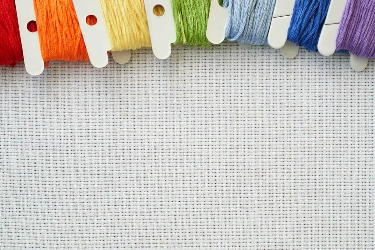 Bobbins with colorful cotton threads for embroidery on white aida cloth