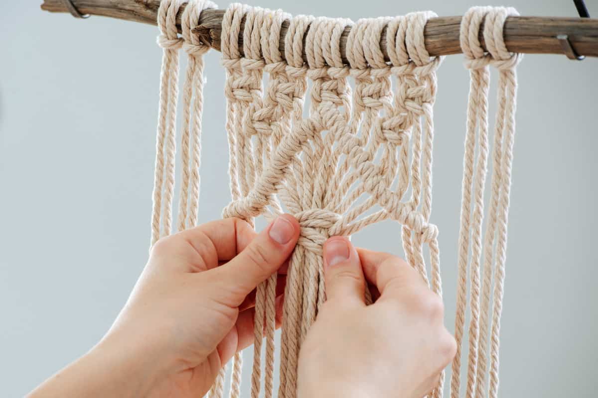 Brunette woman working on a half-finished macrame piece, weaving ropes, making knots
